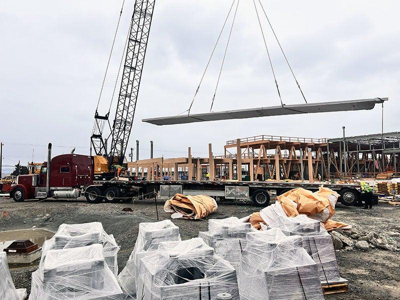 a crane is lowering a large sheet of wood onto a wood frame of a building under construction